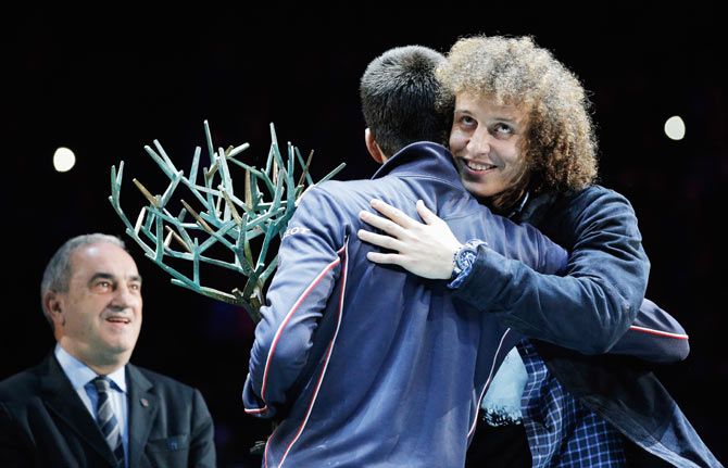 Paris Saint Germain's Brazilian footballer, David Luiz (right) embraces Novak Djokovic as he hands him the Paris Masters trophy 