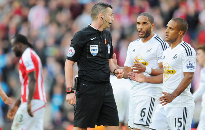Swansea player Wayne Routledge (right) and Ashley Williams (centre) confront referee Michael Oliver after Stoke City's Victor Moses (left) was awarded a controversial penalty on Sunday