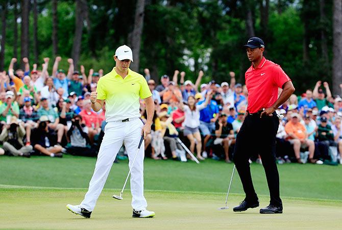 Rory McIlroy of Northern Ireland celebrates a birdie putt on the 18th green as Tiger Woods of the United States looks on