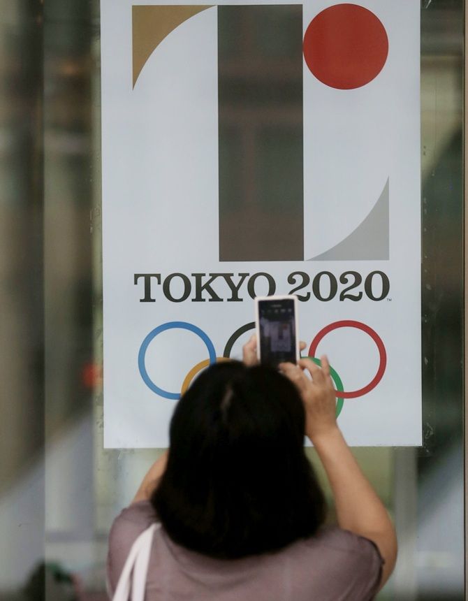 A woman takes a photograph of a poster showing the Tokyo 2020 Olympic logo 