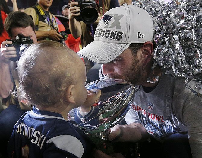 New England Patriots kicker Stephen Gostkowski kisses the Vince Lombardi Trophy with his youngest son after the NFL Super Bowl XLIX football game