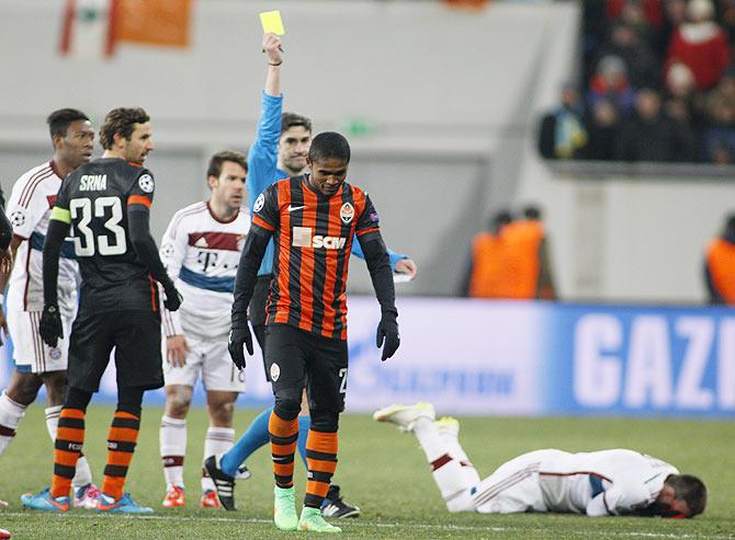 Match referee Alberto Undiano Mallenco shows a yellow card to Shakhtar Donetsk's Douglas Costa (centre) after he fouled Bayern Munich's Franck Ribery (right, on the ground)