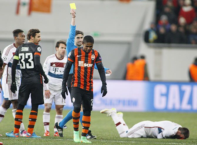 Match referee Alberto Undiano Mallenco shows a yellow card to Shakhtar Donetsk's Douglas Costa (centre) after he fouled Bayern Munich's Franck Ribery (right, on the ground)