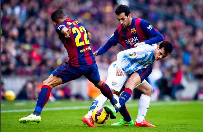 Malaga'a Juanmi Jimenez is challenged by FC Barcelona's Sergio Busquets and Dani Alves