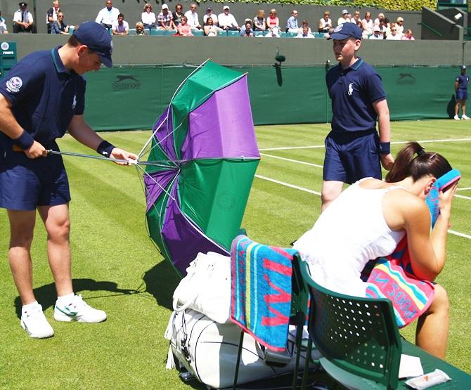 A ballboy adjusts an umbrella as Jelena Jankovic of Serbia takes a break