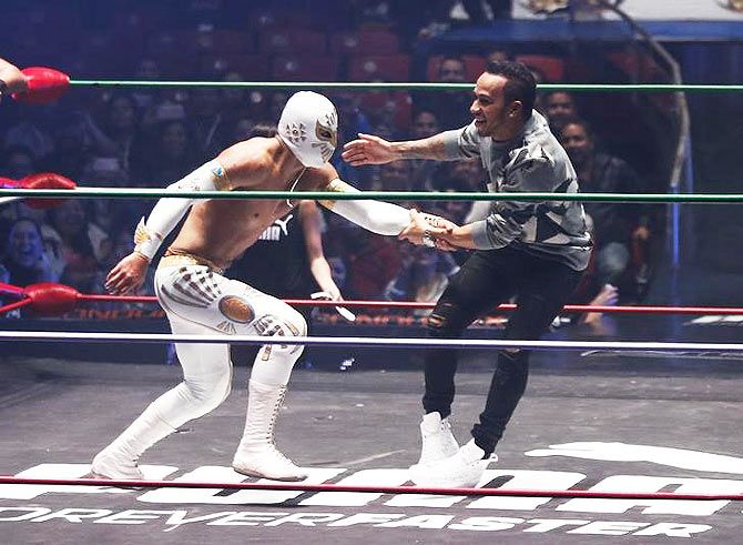 Mercedes' British F1 driver Lewis Hamilton (right) performs with Mexican wrestlers at the Coliseo Arena during a promotional event in Mexico City on October 29