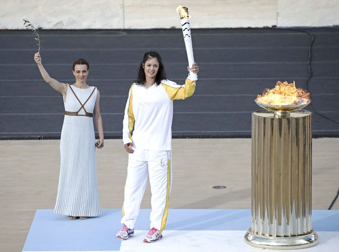Greek rowing World Champion Katerina Nicolaidou (centre), holds a torch after lighting a cauldron with the Olympic Flame during the handover ceremony of the Olympic Flame to the delegation of the 2016 Rio Olympics, at the Panathenaic Stadium in Athens on Wednesday