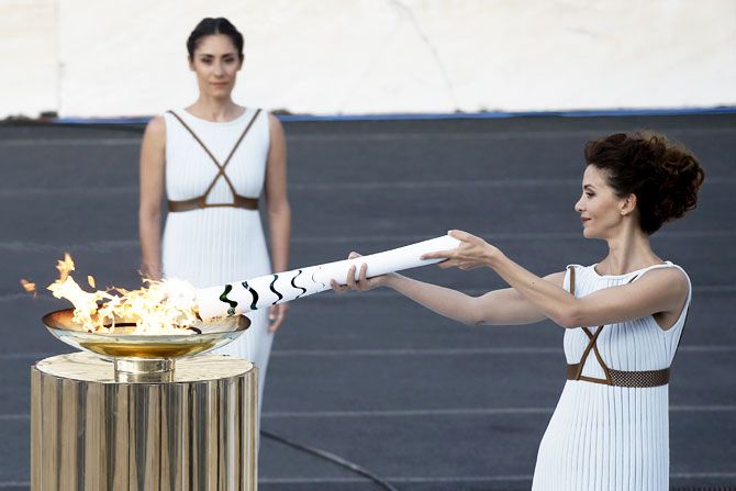 Greek actress Katerina Lehou (right), playing the role of High Priestess, lights an Olympic torch during the handover ceremony of the Olympic Flame to the delegation of the 2016 Rio Olympics, at the Panathenaic Stadium in Athens, Greece, on Wednesday