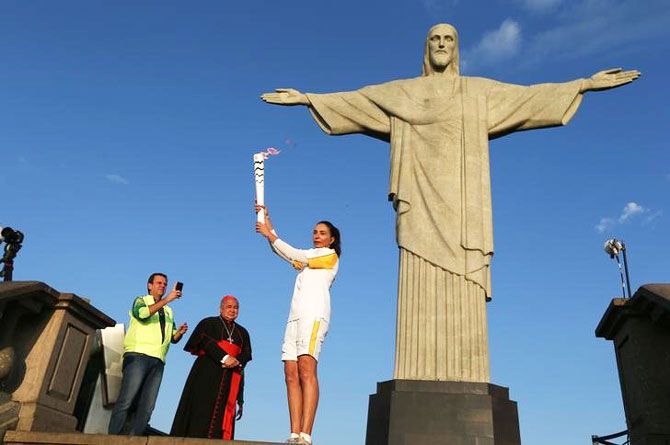 Former Brazilian volleyball player Isabel Barroso holds the Olympic torch next to Christ the Redeemer statue watched by Rio Mayor Eduardo Paes (L) and archbishop Orani Joao Tempesta in Rio de Janeiro on Friday
