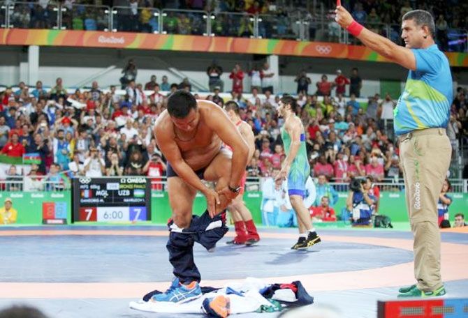 The coach of Mongolia's Mandakhnaran Ganzorig takes off his clothes as he protests after the match against Uzbekistan's Ikhtiyor Navruzov during the Men's Freestyle 65 kg Bronze medal wrestling match on Sunday