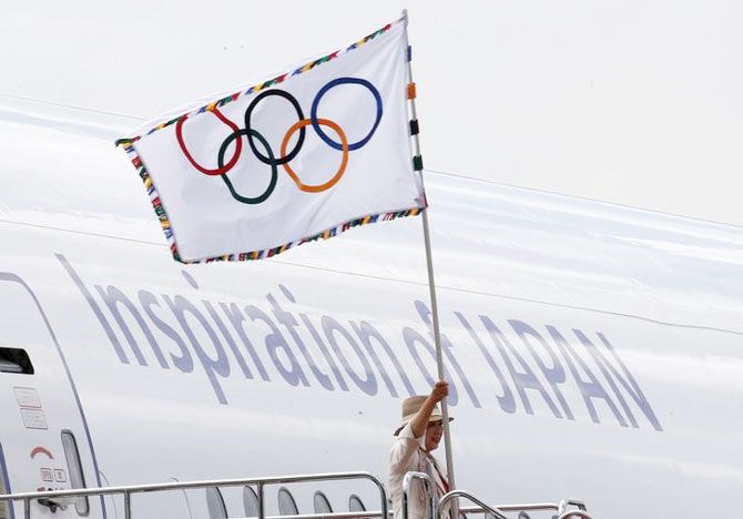 Tokyo governor Yuriko Koike waves the Olympic flag as she walks out of a plane during a ceremony to mark the arrival of the Olympic flag at Haneda airport in Tokyo, Japan, on Wednesday