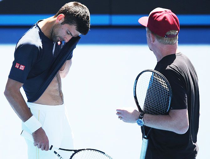 Novak Djokovic wipes away sweat as he talks with coach Boris Becker during a practice session
