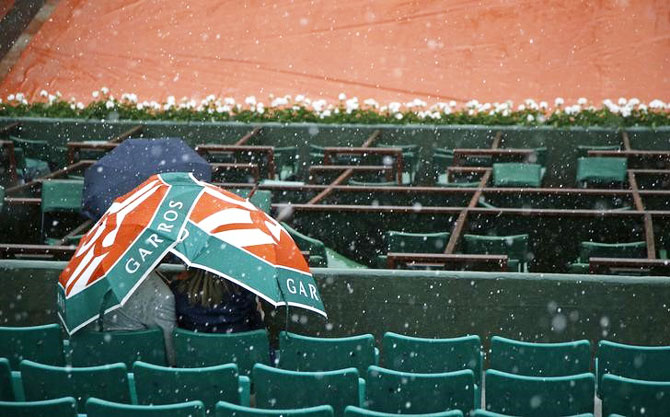 Spectators take shelter under an umbrella during heavy rain falls on Central court at Roland Garros