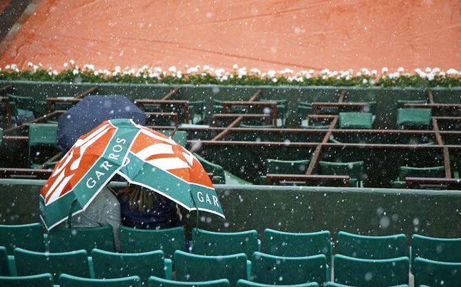 Spectators take shelter under an umbrella during heavy rain falls on Central court at Roland Garros on Thursday
