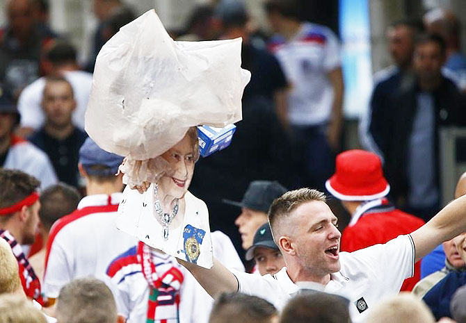 A garbage bag, thrown amongst fans, flies over a cutout of Britain's Queen Elizabeth II as fans celebrate their team's win over Wales in Lille
