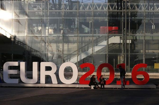 People stand in front of a sign announcing the UEFA Euro 2016 tournament near the Lille Europe railway station in Lille, France