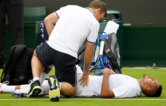 An injured Nick Kyrgios of Australia is given treatment during the Gentlemen's Singles first round match against Pierre-Hugues Herbert of France on Monday