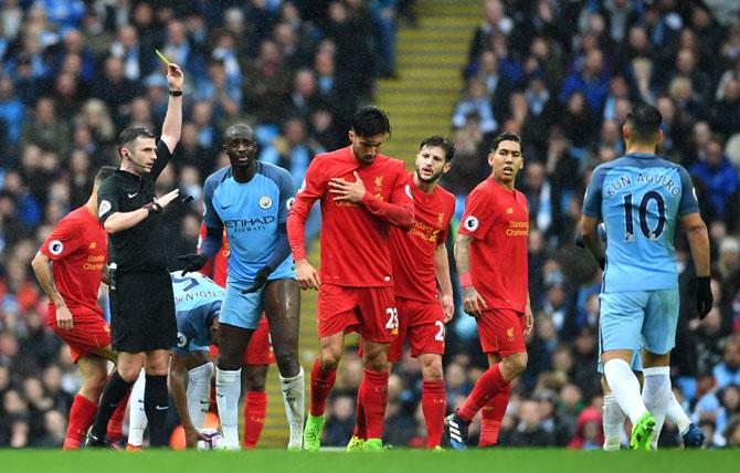 Manchester City's Yaya Toure (C) is shown a yellow card by referee Michael Oliver (left) during the Premier League match between Manchester City and Liverpool at Etihad Stadium in Manchester on Sunday