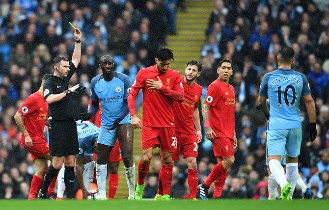 Manchester City's Yaya Toure (C) is shown a yellow card by referee Michael Oliver (left) during the Premier League match between Manchester City and Liverpool at Etihad Stadium in Manchester on Sunday
