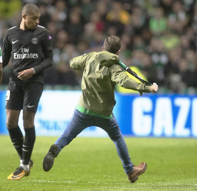 A Celtic fan runs on to the pitch and aims a kick at Paris Saint Germain's Kylian Mbappe during the UEFA Champions League match at Celtic Park Stadium in Glasgow, on Tuesday