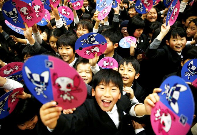 School students hold paper fans featuring the mascot for the Tokyo 2020 Olympics and Paralympics at the Hoyonomori Gakuen School in Tokyo on Wednesday