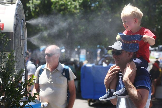 A father and his kid stand before the misting fan to find respite from the heat