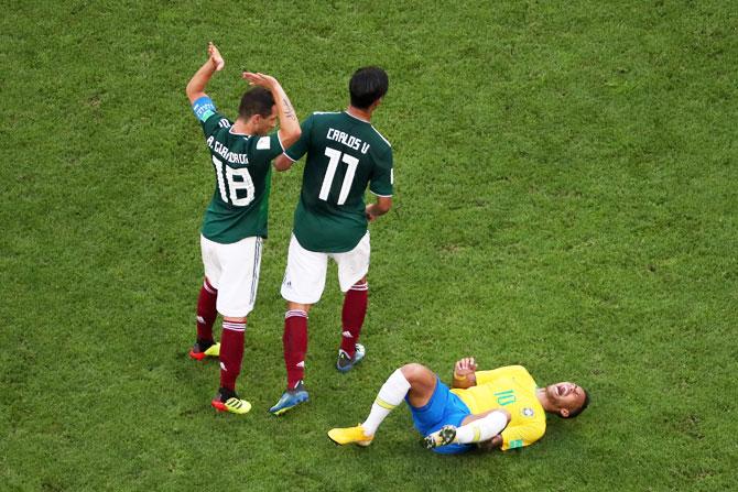 Neymar Jr of Brazil lies on the pitch injured while Andres Guardado and Carlos Vela of Mexico pass by 