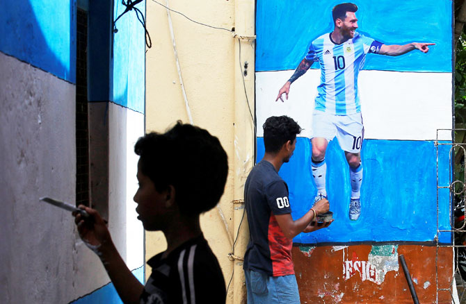 A boy paints a wall with the colours of Argentina's flag next to a man giving finishing touches to a cut-out of soccer player Lionel Messi after pasting it on a wall in an alley in Kolkata on June 10