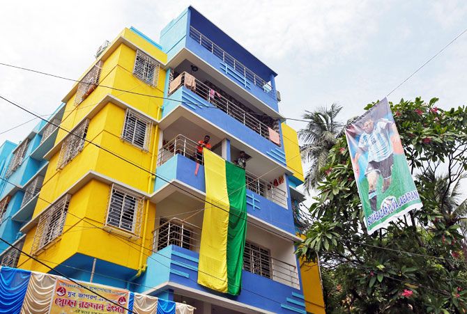 Fans hang a large flag from a residential building next to a banner featuring Argentina's soccer player Lionel Messi in Kolkata on June 10