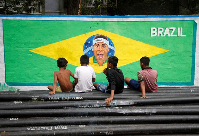 Boys sit on pipes in front of an image of Brazil's soccer player Neymar, painted on a wall, along a road, in Kolkata on June 4