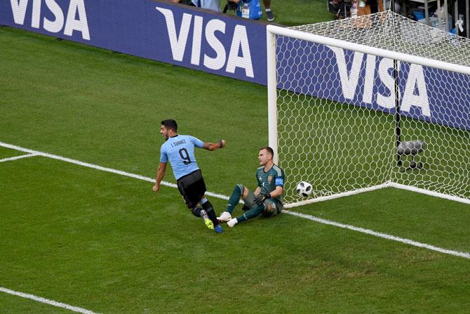 Russia's keeper Igor Akinfeev sits dejected as Luis Suarez celebrates a goal on Monday