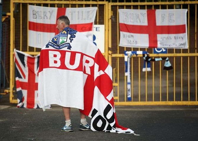 A Bury FC fan wears a flag outside the stadium.