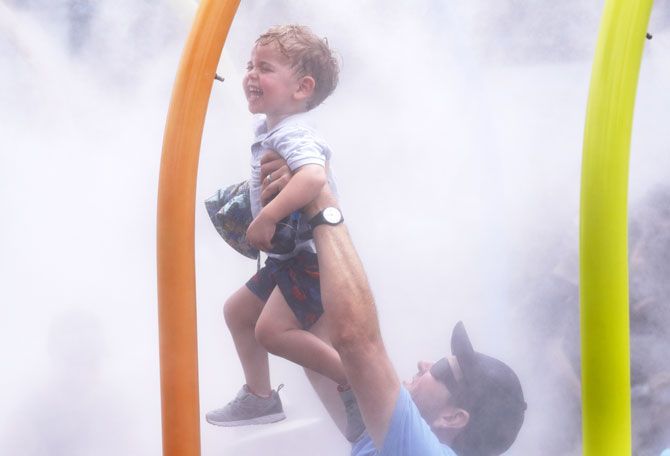 A spectator holds up a child at a water spray to cool down during the Australian Open on Tuesday, January 15