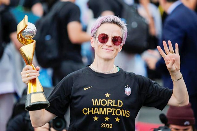 Megan Rapinoe gestures the number 4 with her fingers as she holds the trophy for the FIFA Women's World Cup while the United States team arrives at the Newark International Airport, in Newark, New Jersey, on July 8