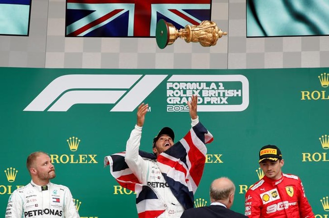 Lewis Hamilton throws the trophy in the air as he celebrates winning the race on the podium, alongside Mercedes's Valtteri Bottas, who finished second, and Ferrari's Charles Leclerc, who finished third.