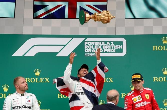 Lewis Hamilton throws the trophy in the air as he celebrates on the podium, alongside Mercedes's Valtteri Bottas, who finished second, and Ferrari's Charles Leclerc, who finished third, after winning the British F1 Grand Prix