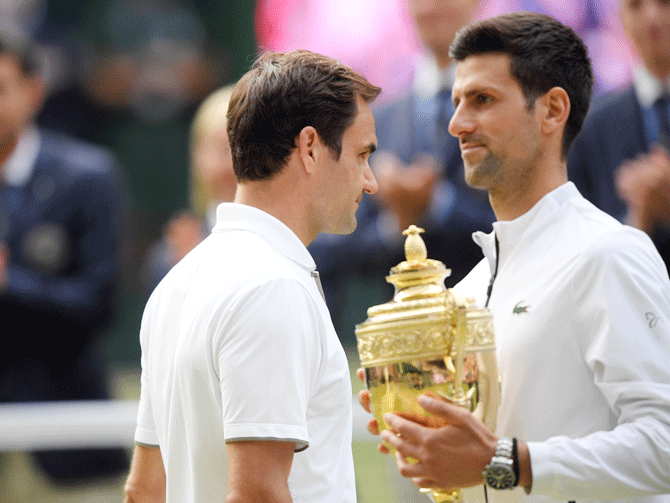 Serbia's Novak Djokovic poses with the trophy after winning the final as Switzerland's as Roger Federer walks past 