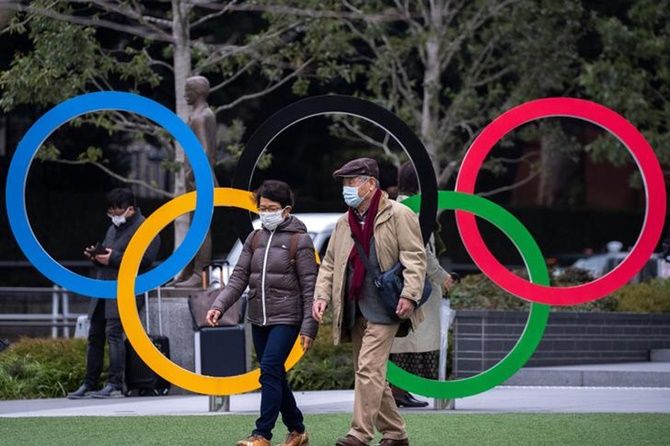 People wearing protective face masks, following the outbreak of the coronavirus, walk past the Olympic rings in front of the Japan Olympic Museum in Tokyo, Japan, on Wednesday.