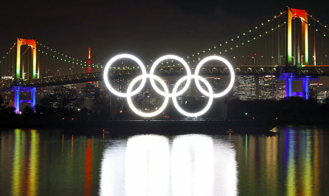 A giant monument of the five interlocking Olympic rings lit up, nestled in the water at Odaiba Marine Park in Tokyo Bay