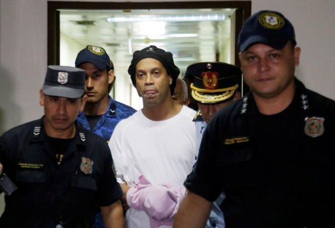 Ex-Barcelona forward Ronaldinho handcuffed and being escorted by police at the Supreme Court of Paraguay.