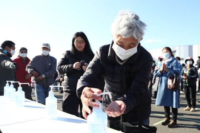 A woman wearing a face mask sanitises her hands prior to queuing to get in front of the Olympic cauldron as the Olympic flame is displayed during the 'Flame of Recovery' special exhibition at Aquamarine Park in Iwaki, Fukushima, Japan, on Wednesday
