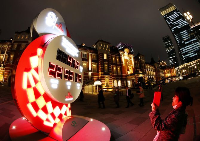 A passerby takes photos of a countdown clock showing the adjusted days and time for the start of the postponed Tokyo Olympic Games, which are now set to begin on July 23, 2021, in front of Tokyo station, in Tokyo on Monday