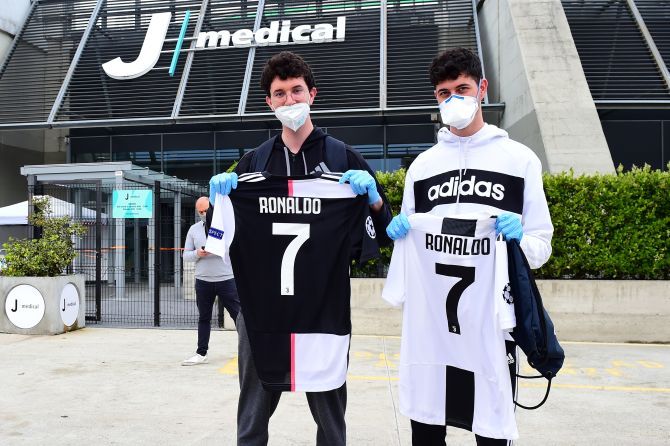 Juventus fans wearing protective face masks and gloves display shirts with Cristiano Ronaldo's name as players and staff arrive for training at Juventus Training Center post the COVID-19 enforced break in Turin, Italy, on Tuesday 