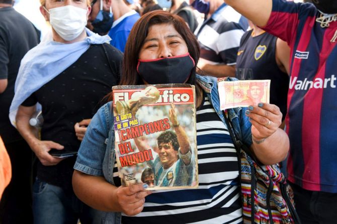 A fan holds a El Grafico magazine of world cup 1986 and a Cuban note bill of Che Guevera as she queues to enter the government palace Casa Rosada to pay her respects to Diego Maradona on Thursday