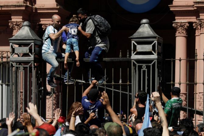Men help a child to climb on the fence of the Casa Rosada presidential palace at Diego Maradona's funeral
