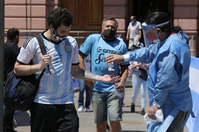 A volunteer puts sanitizing gel on a fan as the former leaves Casa Rosada during Diego Maradona's funeral on Thursday