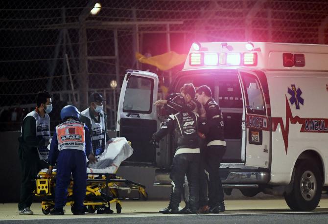 Romain Grosjean limps out as he is helped by FIA doctors to an ambulance