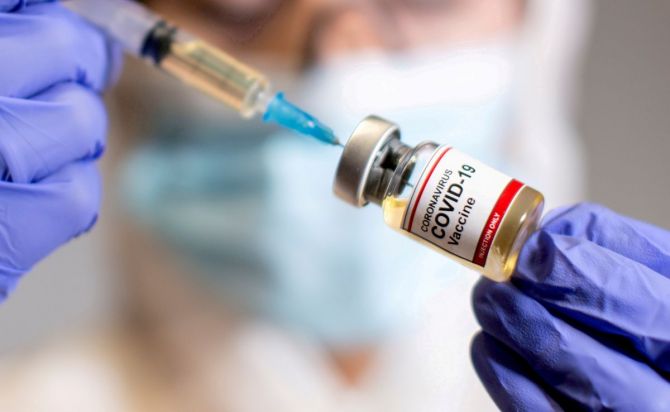 A woman holds a small bottle labeled with a "Coronavirus COVID-19 Vaccine" sticker and a medical syringe in this illustration taken October 30, 2020