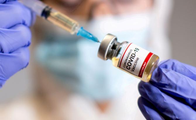 A woman holds a small bottle labeled with a "Coronavirus COVID-19 Vaccine" sticker and a medical syringe in this illustration taken October 30, 2020