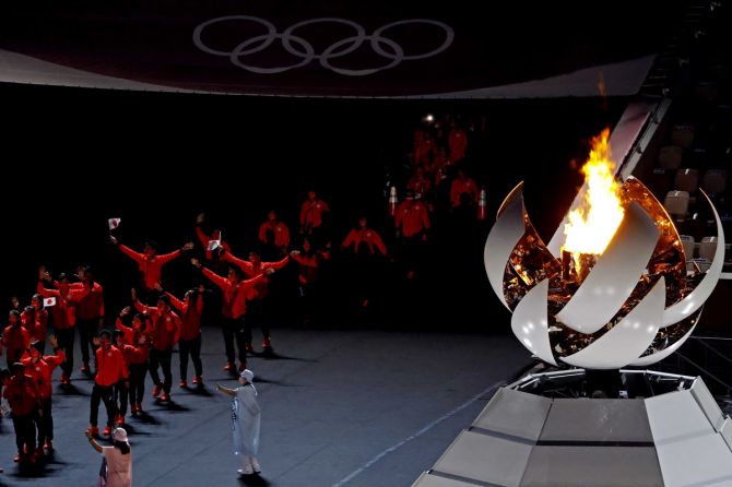 Athletes walk past the Olympic flame at Olympic Stadium before festivities commence during the closing ceremony.